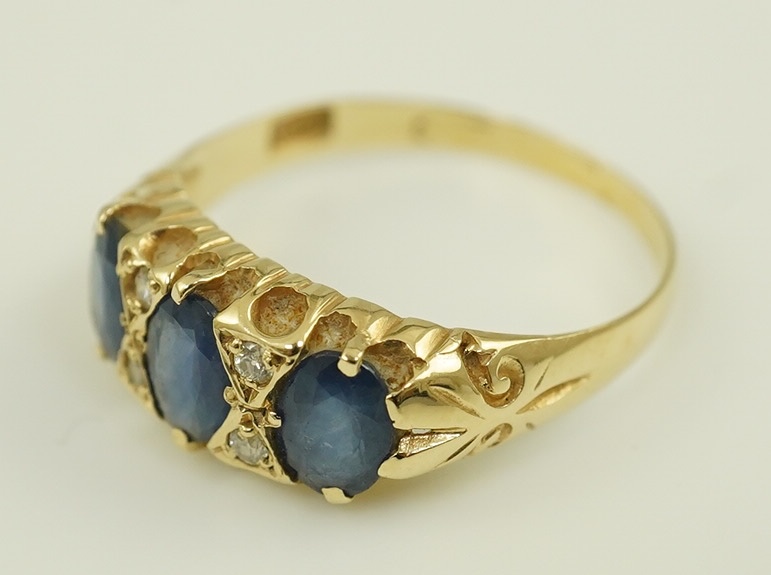 An Edwardian 15ct gold and three stone oval cut sapphire set half hoop ring